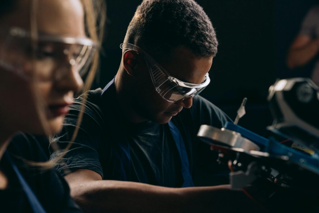 pexels-photo-9242837-9242837 Students focused on robotics, wearing protective goggles, symbolizing teamwork and education in technology.
